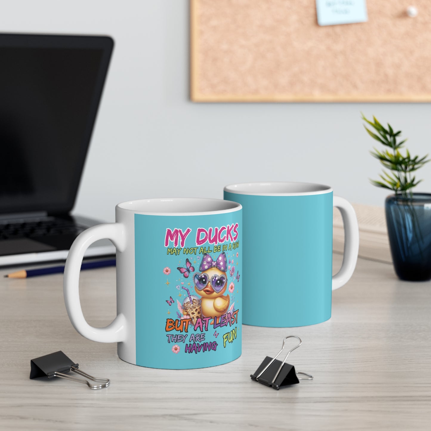 Two mugs on a desk with one featuring a duck design and text.