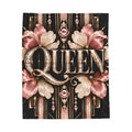 A rectangular decorative blanket featuring the word "QUEEN" in large ornate metallic lettering, surrounded by pink and beige Art Deco-style flowers and geometric details on a black background, shown against a plain white studio backdrop.