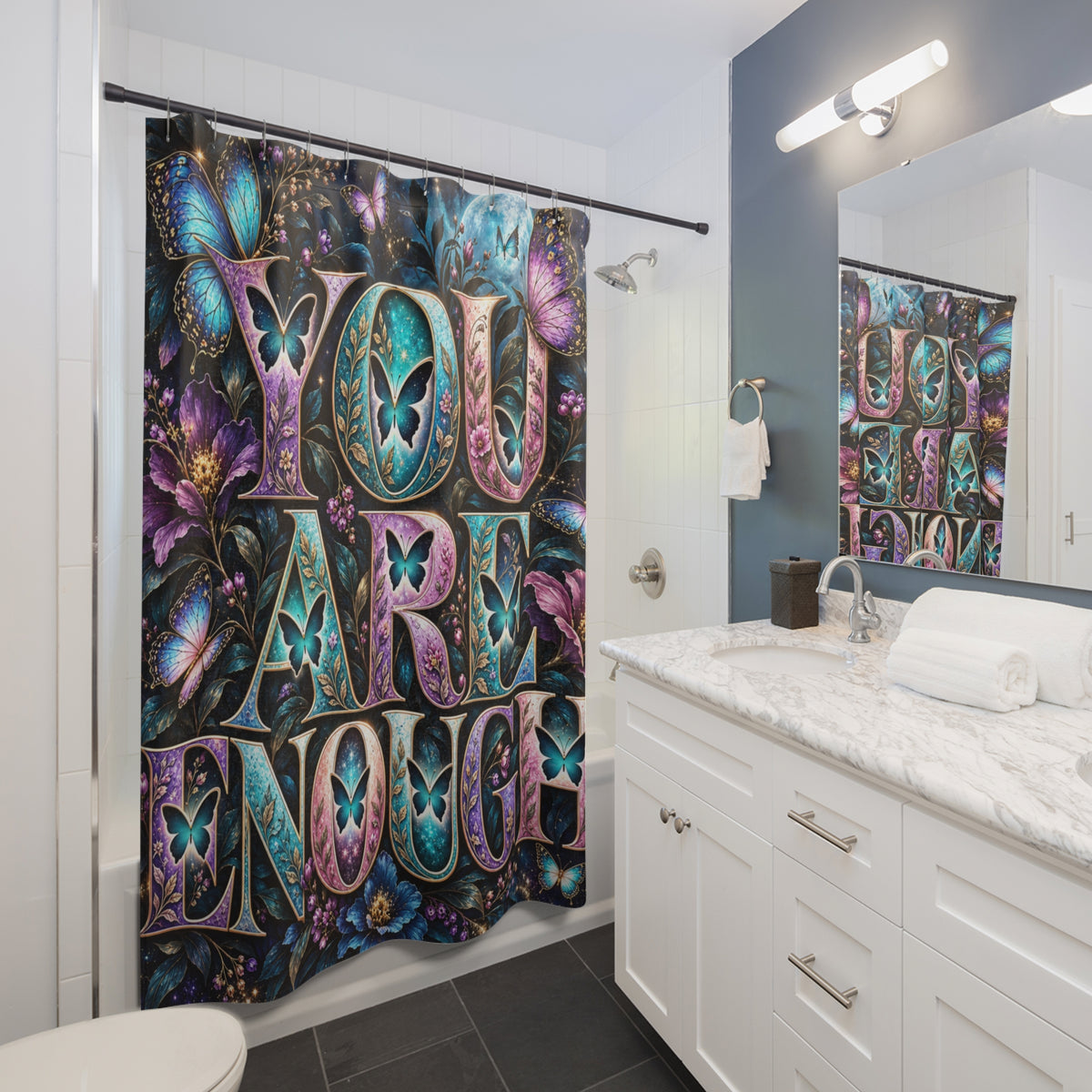 A colorful shower curtain hanging in a modern bathroom. The curtain features large stylized text reading 'YOU ARE ENOUGH' in purple, teal, pink, and gold tones, surrounded by butterflies and floral motifs.