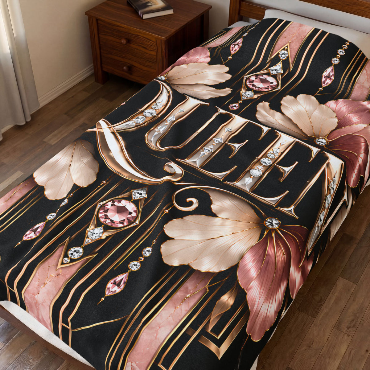 A bedding set featuring a bold graphic print with the word 'QUEEN' in large gold letters, surrounded by pink and gold floral motifs, diamonds, and geometric stripes on a black background, styled on a bed in a bedroom.