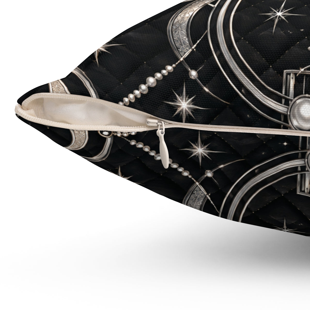 Close-up of a black quilted pillow with a silver celestial pattern of stars, crescent moons, and pearl-like beads, shown with a white zipper pull.