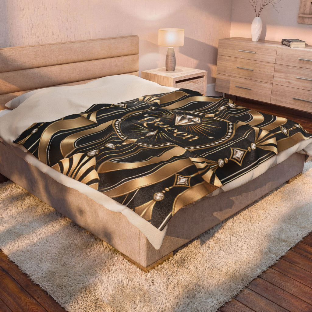 A bed in a styled bedroom setting with a black and gold patterned throw blanket featuring a central diamond motif and the word 'RUGS'.