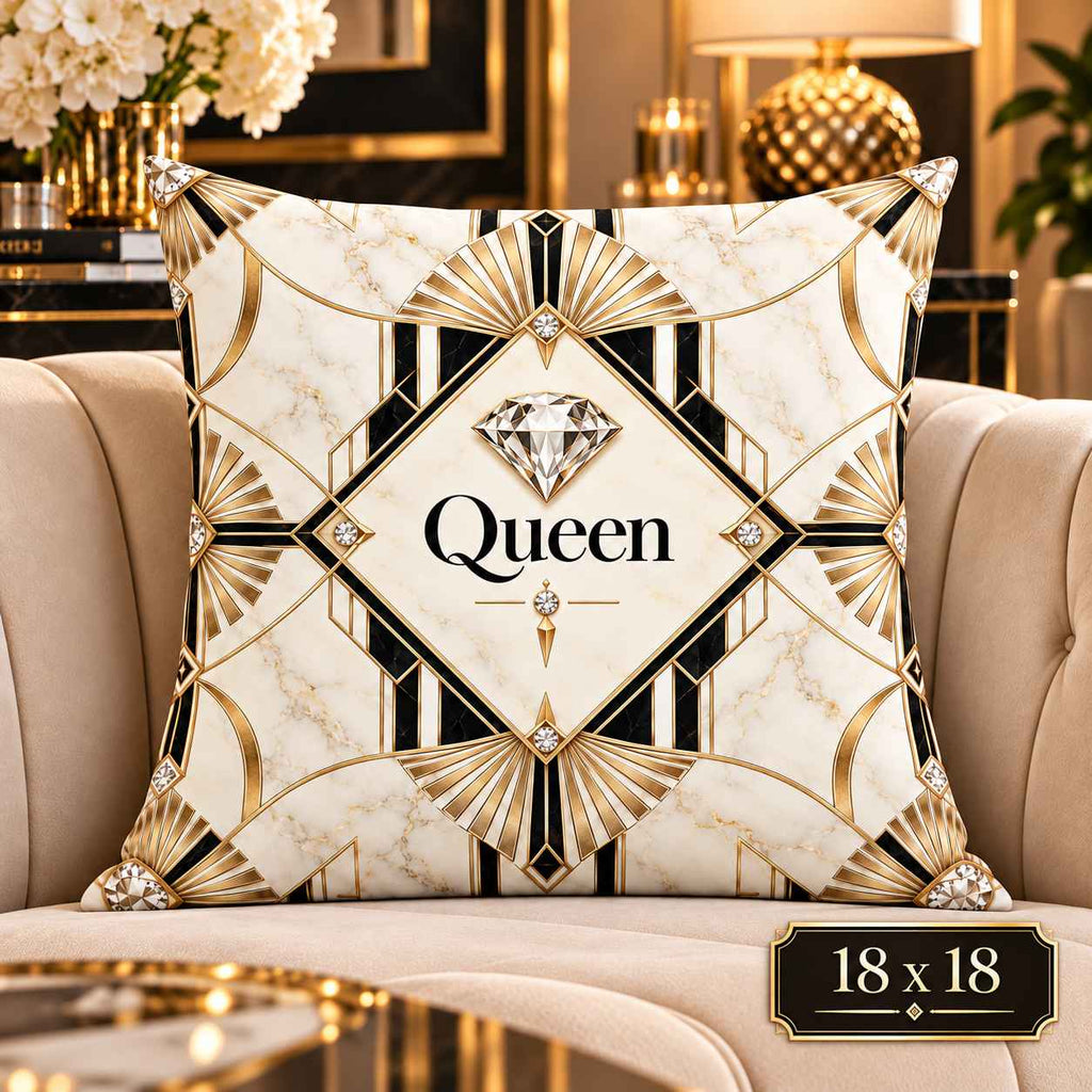 A square decorative throw pillow with an Art Deco style design in cream, black, and gold, featuring a central diamond graphic and the word 'Queen' printed in the middle. The pillow is displayed on a beige armchair in a luxurious, high-end living room setting with gold furniture and lamps.