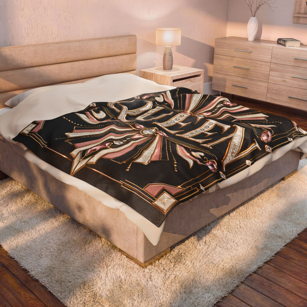 A patterned throw blanket draped over a bed in a modern bedroom setting. The blanket features a black background with a detailed geometric and tribal-inspired design in beige, pink, and gold.