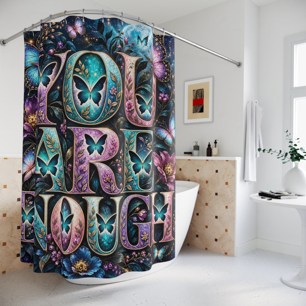 A colorful shower curtain hanging in a bright white bathroom. The curtain features large decorative letters spelling 'YOU ARE LOVED' with butterfly motifs and floral artwork in teal, purple, pink, and blue tones.