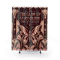 A shower curtain featuring an Art Deco style design with a large jeweled butterfly and the text 'THE GLOW-UP STARTS BEHIND THIS CURTAIN' on a dark brown background, shown hanging in a studio setting.