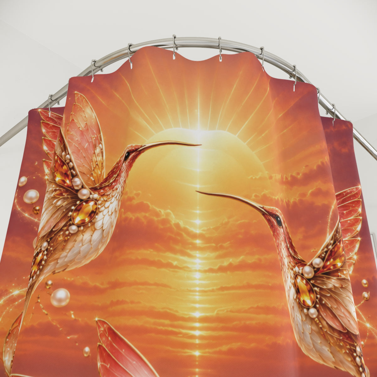 A shower curtain panel with a vivid printed design of two hummingbirds in front of a glowing orange and yellow sunburst sky, suspended from a curved metal rod against a plain light background.
