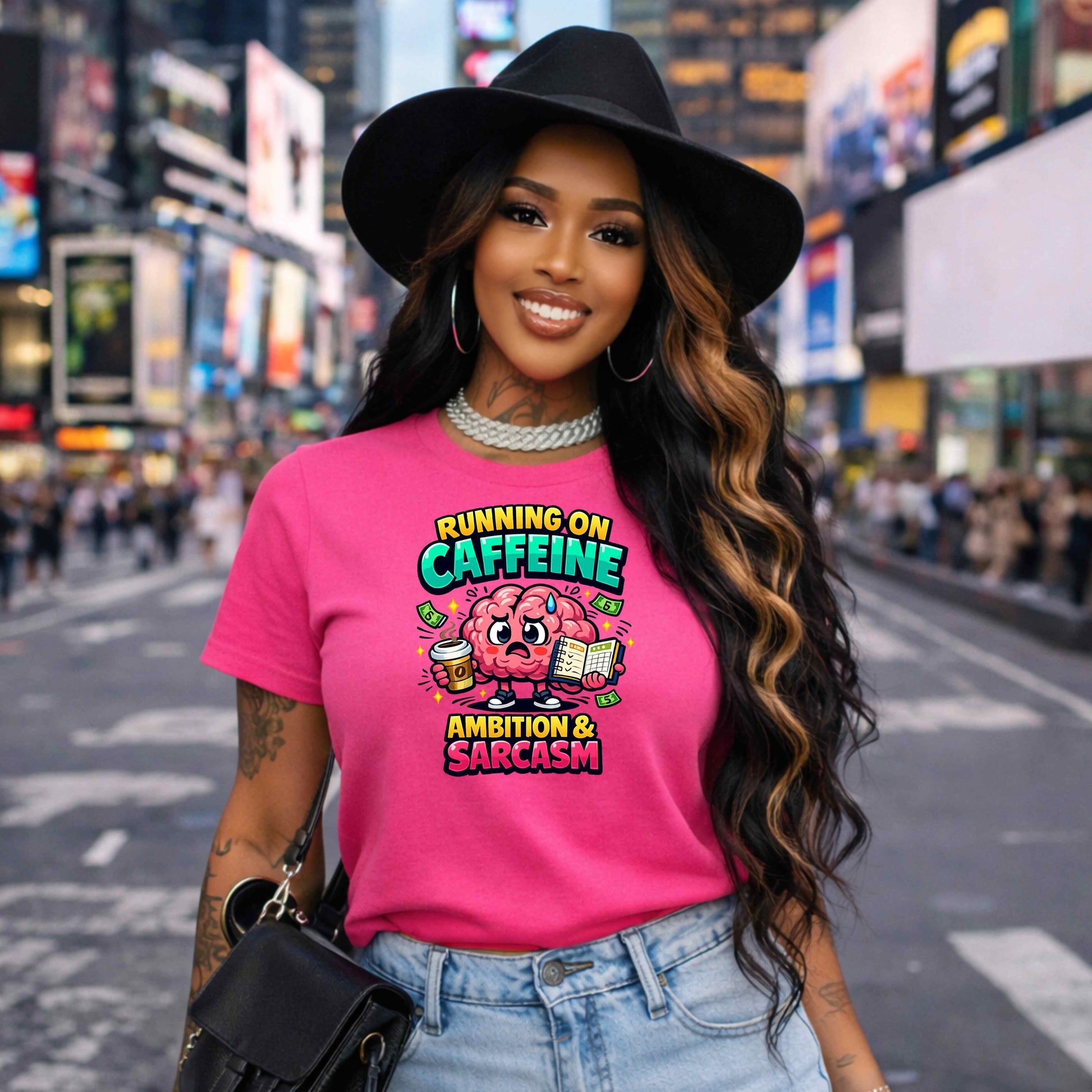 Woman wearing a pink t-shirt with a graphic design a colorful graphic of a brain holding a coffee cup and books, with text 'Running on caffeine, ambition & sarcasm