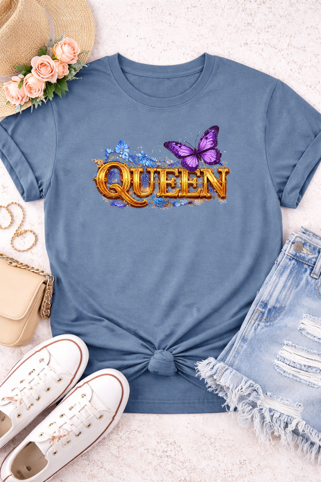 Blue t-shirt with 'QUEEN' text and butterfly graphic, surrounded by accessories on a light surface.