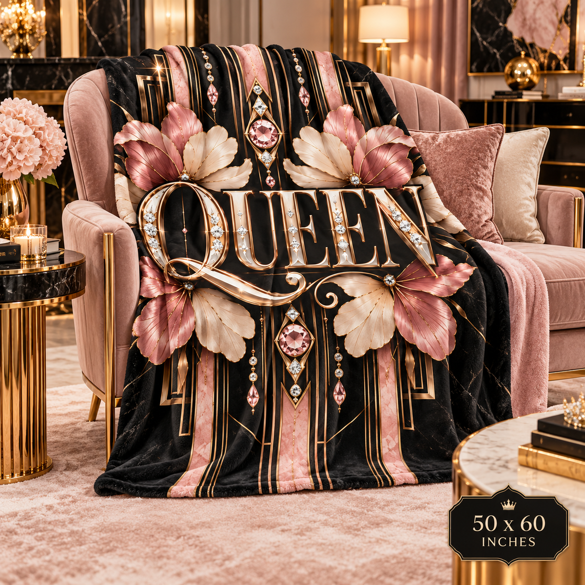 A plush throw blanket draped over a pink velvet armchair in a luxurious room. The blanket features a black velvet base with vertical pink and gold stripes, large metallic pink and gold floral motifs, and the word 'QUEEN' in raised gold letters with jeweled details.