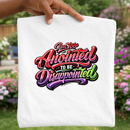 White T-shirt with colorful text 'I'm too Anointed To be Disappointed' held by a hand with a garden background